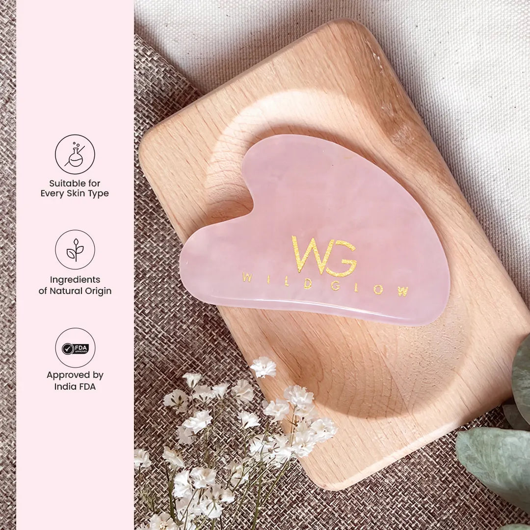 A pink rose quartz gua sha massage tool with gold foil 'WG MISSION' branding, resting on a wooden tray. The left side features a pink vertical banner with product feature icons and text, and the background includes neutral fabric and small white flowers.