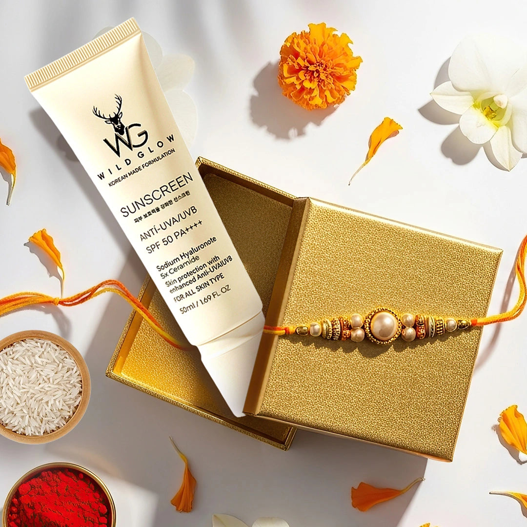 Wild Glow Sunscreen tube displayed next to a gold box with a beaded rakhi on top, styled with orange marigold petals, white rice, red powder, and a white flower on a white background.